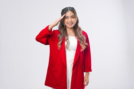 Smiling Indonesian woman wearing red jacket is doing salute gesture, isolated by white background.