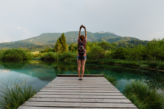 A female traveler arms outstretched while standing on a wooden path beside an emerald lake. Vitality and eco-tourism concept showcasing physical well being immersed in a pristine environment.
