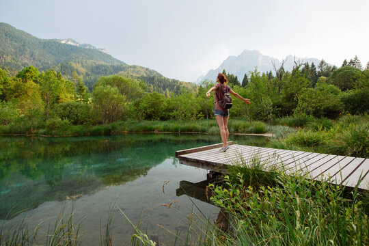 A female traveler arms outstretched while standing on a wooden path beside an emerald lake. Vitality and eco-tourism concept showcasing physical well being immersed in a pristine environment.