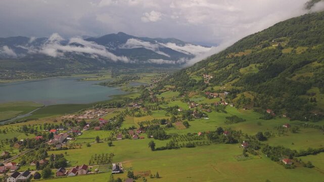 Wide aerial view of Plav town and Lake Plav under dramatic cloudy sky near Prokletije mountains, Montenegro.