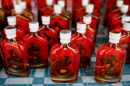 Bottles of traditional snake wine on a market table, preserved snake in red liquor, exotic souvenir display.