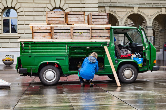 Worker Unloading Wooden Crates from Green Utility Truck on Wet Street