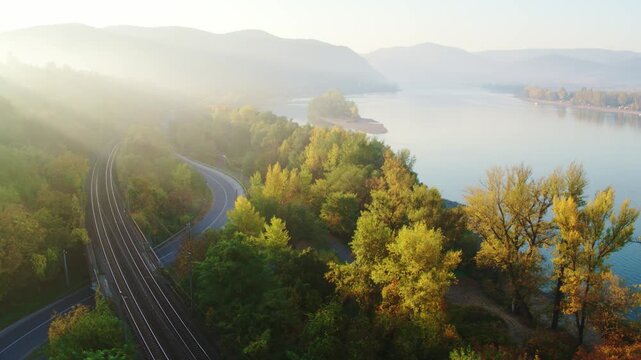 Aerial view of sunbeams shining through mist over a road and railway by the Danube