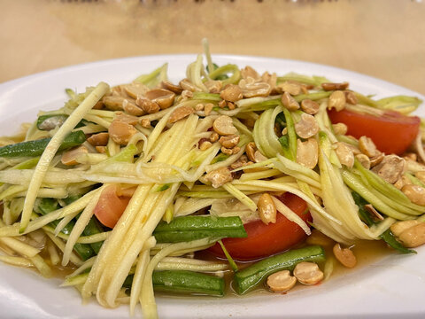Fresh Thai-style green mango salad with shredded mango, vegetables, peanuts, and spicy dressing served on a plate.