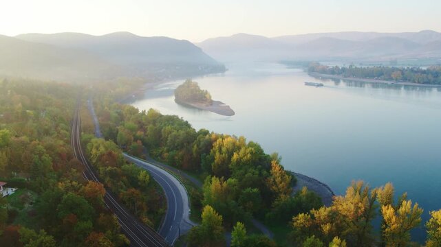 Wide aerial view of the misty Danube river with winding coastal road and railway in autumn