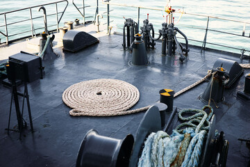 Coiled mooring rope neatly arranged on a steel ship deck beside winches and bollards, nautical...