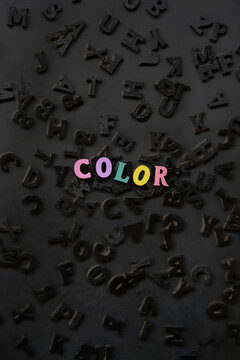 word "color" made of colorful letters and  many black alphabet letters randomly scattered on abstract black background close up. element for creative project and modern design. minimal style