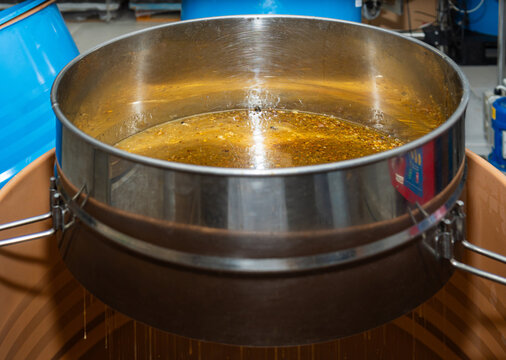 Raw honey filtering through a stainless steel sieve