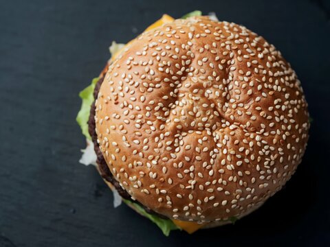 Freshly baked sesame seed burger bun with golden crust on dark slate background