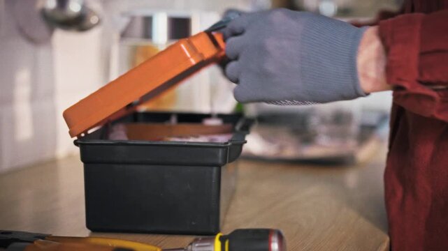 A technician in gloves and work uniform carefully places a toolbox on a kitchen table in a bright home setting. Concept of professional home repair and on-site appliance maintenance service