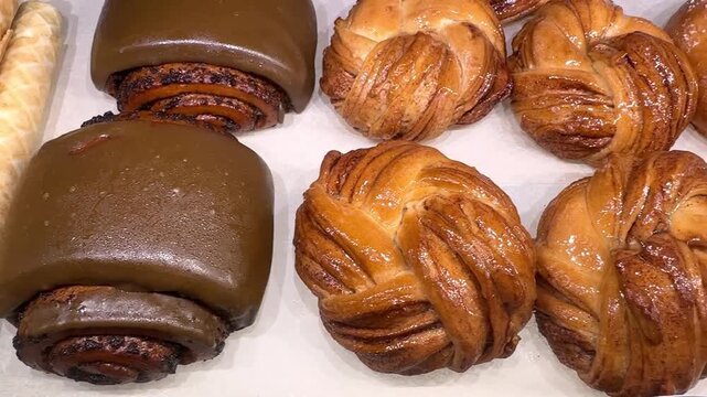 A close-up view of traditional Scandinavian bakery pastries featuring golden brown twisted Swedish cinnamon buns (kanelbulle) and rich chocolate-glazed buns arranged on white parchment paper. 