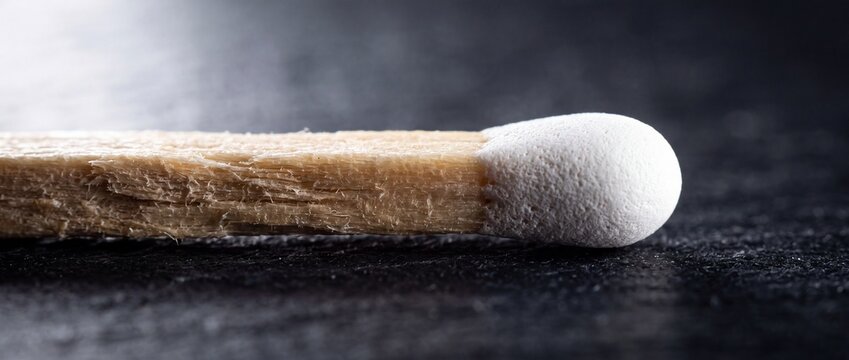 Macro view of white unlit matchstick head showing detailed texture of chemical coating and wooden stick fibers on dark textured surface for fire safety concept.