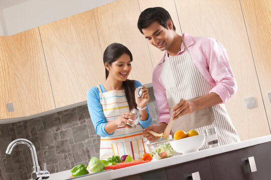Smiling young couple preparing fresh salad in kitchen