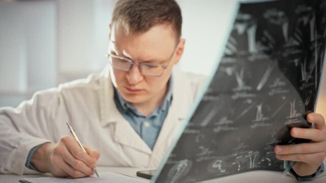 In hospital imaging suite, medical specialist reviews a large MRI film with multiple angled images, entering the patient's condition into the medical record to guide fracture diagnosis and treatment