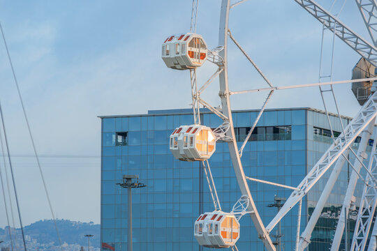 White Ferris Wheel Cabins with Modern Glass Building, Amusement Park Attraction, Cityscape Sky View