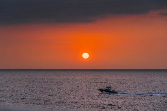 Police Patrol Boat Sailing on the Sea During Vibrant Orange Sunset, Guardia Civil, Small Speedboat Navigating CalmAquatic Waters, Golden Hour Coast