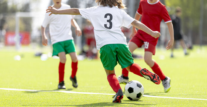 Young Soccer Player in Number 3 White Shirt and Green Shorts Striking Ball During Competitive Match - Action Shot on Grass Pitch