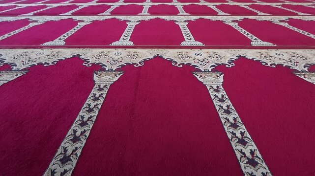 Symmetrical rows of red patterned prayer carpet inside mosque