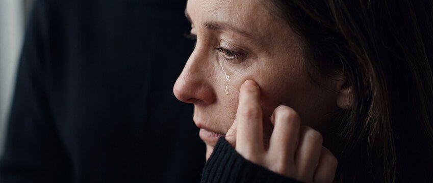 Woman crying with single tear rolling down cheek touching face with hand sad expression emotional portrait darkness low light dramatic scene personal struggle.