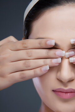 Close-up of a young woman covering eyes with hands over colored background 