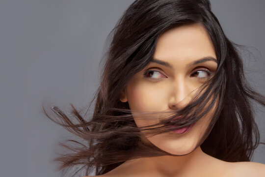 Pretty young female with hair blowing over face against colored background 