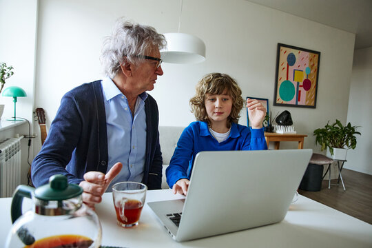 Senior man and teenage boy talking together while sharing a relaxed day at home