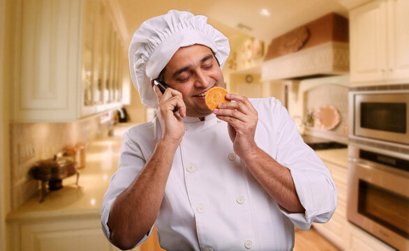 Chef talking on a mobile phone and smelling a cookie 
