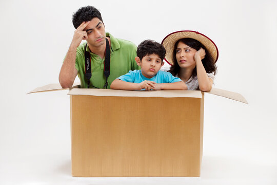 Bored young couple sitting inside cardboard box with little son 