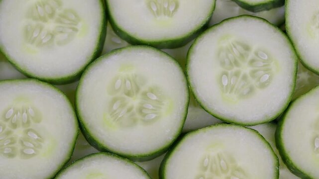 Thinly sliced cucumbers with dewy surface forming repetitive decorative motif. Closeup of cucumber segments arranged in repeating pattern showcasing dew and vibrant green hues