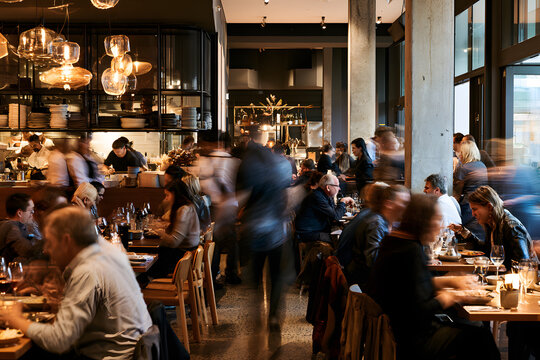 An active dining scene, with customers seated at tables and servers going about their work, a crowded area with people in motion
