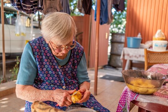 Elderly woman peeling potatoes outdoors for traditional home cooked dinner