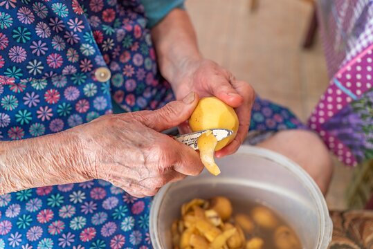 Close up of elderly woman wrinkled hands peeling raw potato