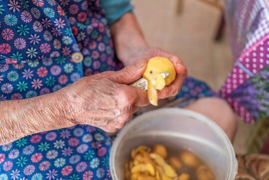 Wrinkled hands of senior woman peeling fresh organic potato closeup