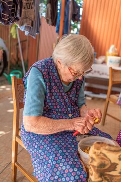 Elderly woman sitting on chair peeling potatoes on terrace side view