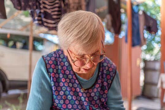 Senior woman in glasses working carefully on outdoor village terrace