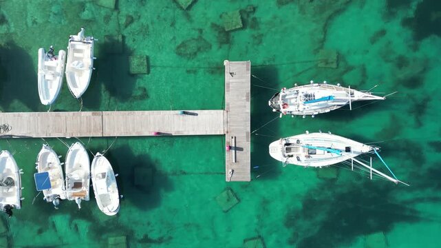 Aerial view of boats docked at a wooden pier in the clear turquoise waters of Otranto, Apulia, Italy.
