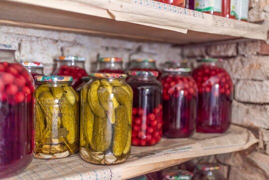 Assorted homemade pickled cucumbers and sweet cherry compote jars on pantry shelf