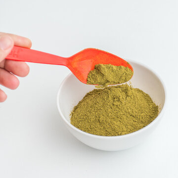 Hand using red measuring spoon to scoop green matcha tea powder from white bowl