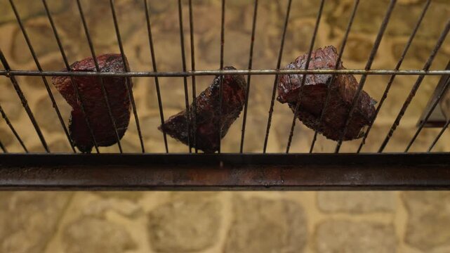 Low angle view from beneath the grate as juices drip from grilled steaks on the bars