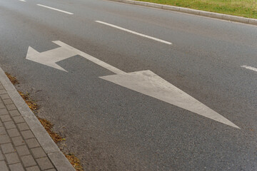 Obraz premium White painted arrow on asphalt road surface showing left and straight traffic direction, typical urban transportation infrastructure element