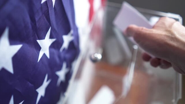 High angle of voter dropping ballot into transparent box with US flag on background