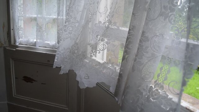 Close-up of delicate white lace curtains gently billowing in a summer breeze at an open traditional vertical sash window. Pre-Georgian period property, no people.