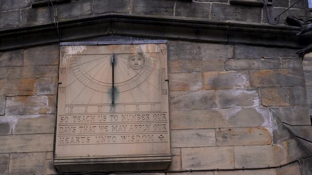 Fixed shot of an old stone sundial with a sun face and biblical inscription mounted high on a weathered wall.