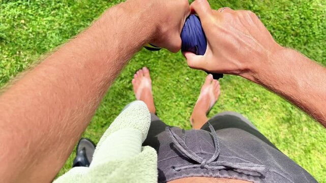A person wrings excess water out of blue swimwear while standing barefoot on green grass. Ideal for summer activities, outdoor recreation, swimwear, and hygiene content.