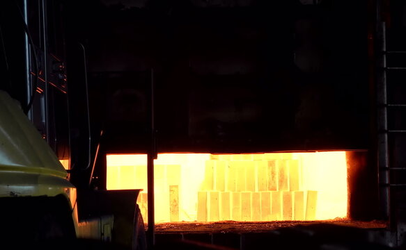 A high-temperature furnace glows bright orange, revealing neatly arranged refractory blocks inside. The intense illumination highlights the heat-resistant materials used for thermal processing in heav