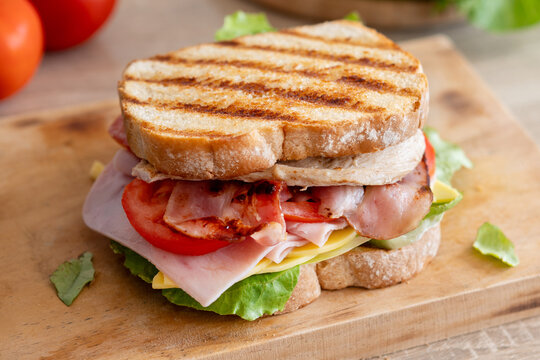 Grilled club sandwich with bacon and ham on wooden table