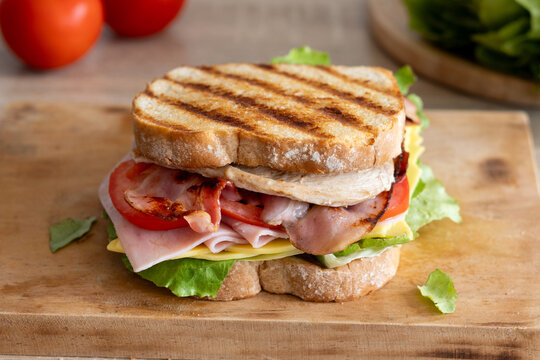 Grilled club sandwich with bacon and ham on wooden table