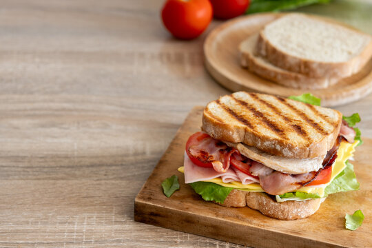 Grilled club sandwich with bacon and ham on wooden table. Copy space