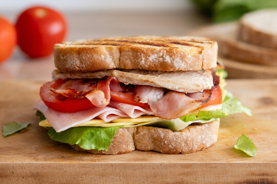 Grilled club sandwich with bacon and ham on wooden table
