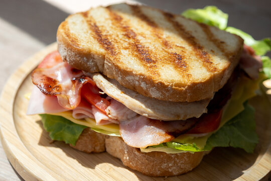 Grilled club sandwich with bacon and ham on wooden table
